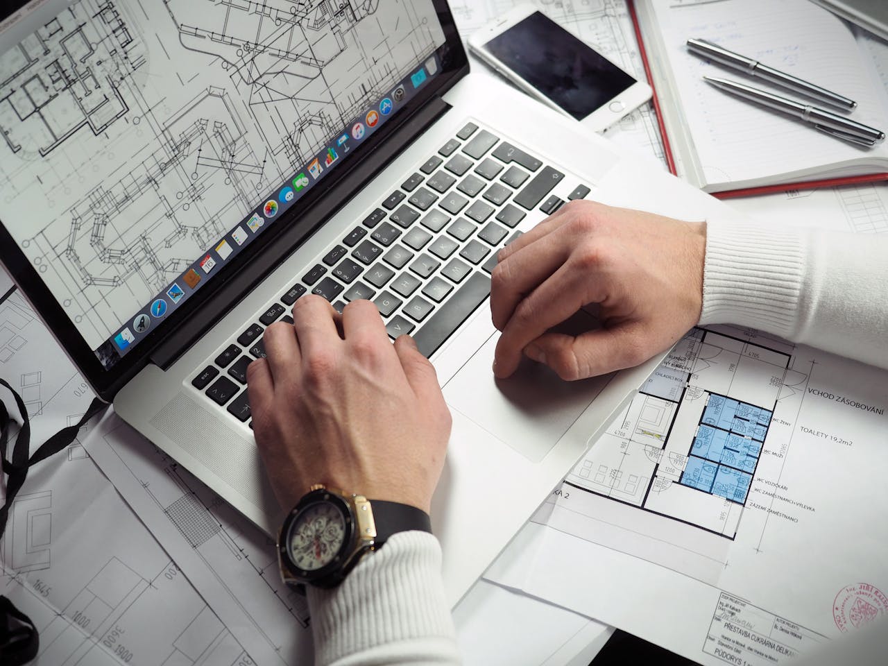 Home Architect reviewing detailed floor plans and schematics on a laptop with a smartphone nearby.